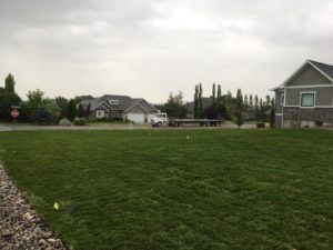 A sod lawn being watered. The flatbed semi truck used to transport the sod is parked on the road on the other side of the lawn.